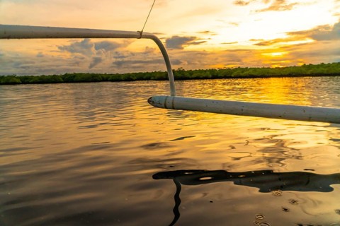 Outrigger of a banca boat sailing on calm water during a golden sunset in siargao island,