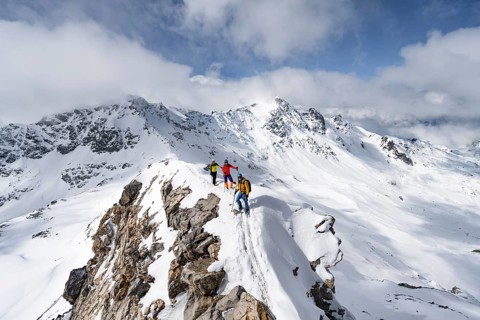 Three mountaineers climbing the narrow ridge of Piz Laviner, view of mountain panorama in winter