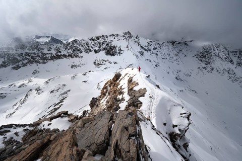 Mountaineer descending the narrow ridge of Piz Laviner, view of mountain panorama in wintry
