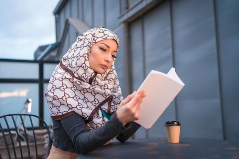 Arab girl with white veil at the computer on the terrace of a coffe shop, having a lot of fun