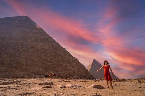 A young girl in a red dress at the pyramid of Cheops the largest pyramid at sunset. The pyramids of