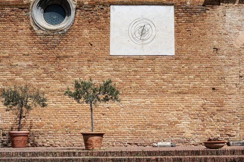 Brick wall with a sundial and two olive trees in a pot on a Mediterranean site, Tuscany, Italy,