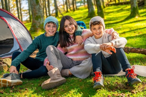 Bothers and sister sitting on the grass in the forest smiling at camera together enjoying camping