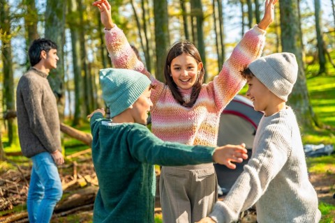Brothers and sister raising hands after stacking while enjoying a camping day with family in a