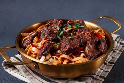Udon noodles with Mongolian beef, green onions and vegetables, in a brass pan, on a gray