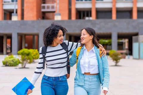 Frontal three quarter length photo of two multi-ethnic female student embracing walking along the