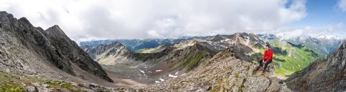 Panorama, mountaineer sitting on a rock, on a steep rocky ridge, on the summit of the Lasörling,