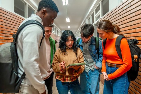 Diverse group of high school students collaborating on a project using a digital tablet in a school