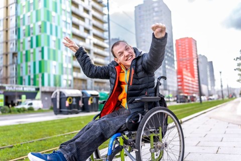 Portrait of a cheerful disabled man raising his arms in celebration, sitting in his wheelchair on a