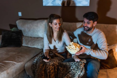 Happy couple sharing popcorn and enjoying a cozy movie night at home, snuggled together on the sofa