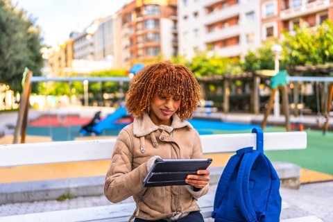 Latin young woman sitting on urban park bench using digital tablet