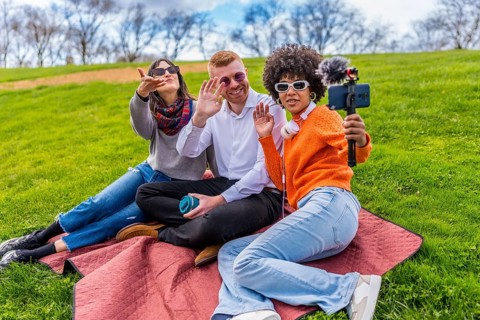 Three content creators waving and filming video with smartphone and external microphone in a park
