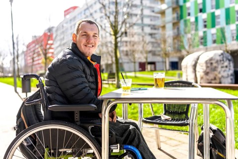 Young man in a wheelchair enjoys a refreshing drink with a friend at a table outside a cafe,