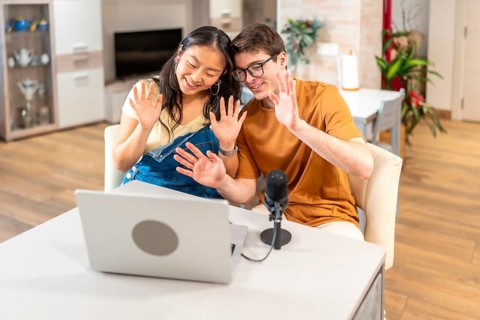 Multiethnic couple of content creators waving at their audience while recording a new episode of