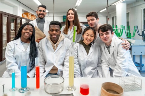 Group of diverse university students and their teacher posing together in a chemistry laboratory,
