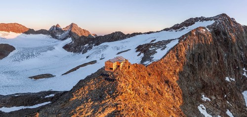 Atmospheric sunrise in a picturesque mountain landscape, alpenglow, aerial view, mountain hut