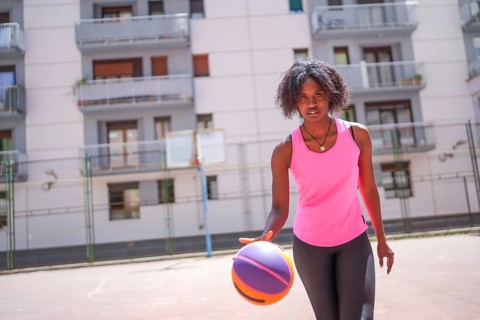 Confident afro woman looking at camera while dribbling in an urban basketball court