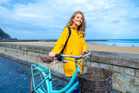 Happy young woman walking with her bicycle on the boardwalk by the beach, enjoying the fresh air