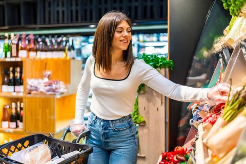 Young woman shopping for groceries, choosing fresh organic vegetables from a display shelf in a