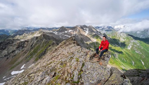 Mountaineer sitting on a rock, on a steep rocky ridge, on the summit of the Lasörling, view of the