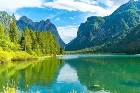 Stunning alpine landscape reflecting on lake dobbiaco's emerald waters, surrounded by lush
