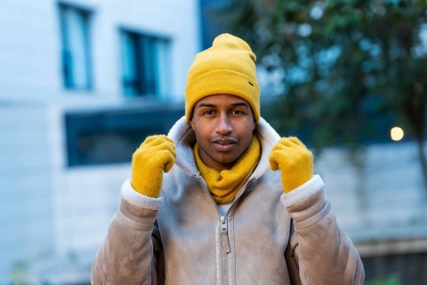 Stylish man wearing a bright yellow hat, gloves, and scarf, braving the cold winter weather while