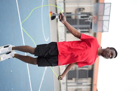 Vertical photo of an energetic african teenager jumping rope in an urban basketball court