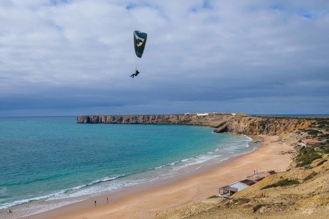 Sagres, Algarve, Portugal - Paraglider flying on the town beach Praia da Mareta, behind the sea