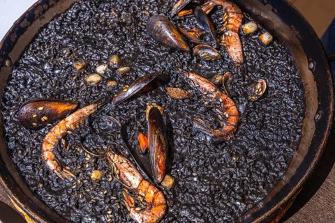 Close up of black paella with shrimps, mussels and other seafood, cooked and ready to be served in