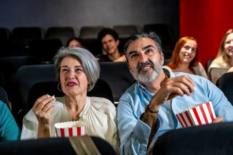 Senior couple watching a movie and eating popcorn, enjoying a night out at the cinema with other