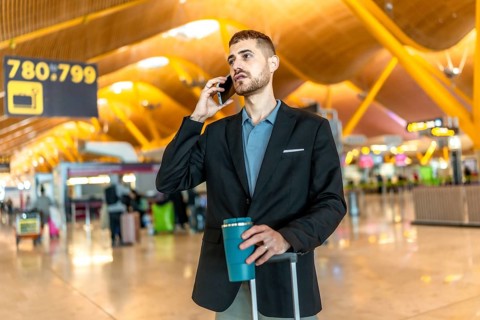 Businessman waiting for his flight, talking on the phone and holding a coffee while pulling his