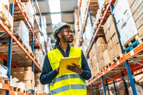 African warehouse supervisor using tablet while working tracking packages and doing inventory