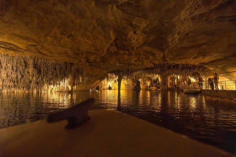 Tourists enjoying a boat trip on the martel lake inside the drach caves, illuminated by colorful
