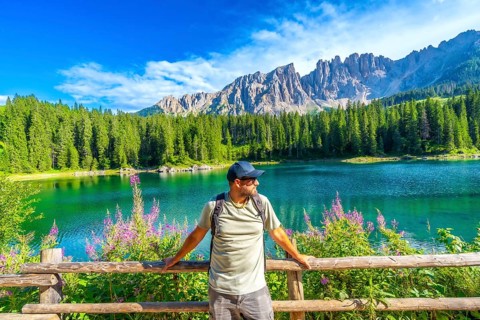 Hiker relaxing by a wooden fence, admiring the stunning turquoise waters of lake carezza with the