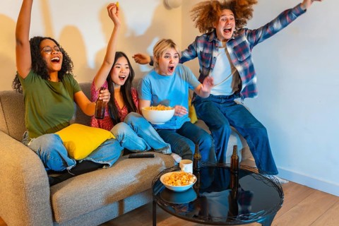 Group of young multi ethnic people enjoying a sports event on television, drinking beer and eating