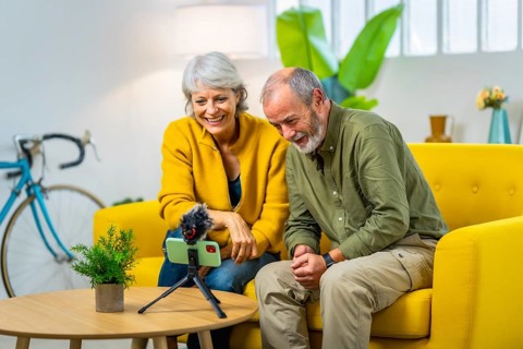 Senior couple doing an online video with family using mobile phone attached to a tripod and mic