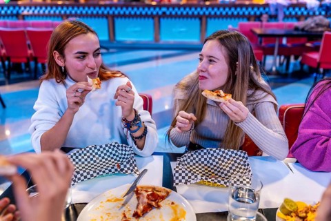 Two friends enjoying pizza at a bowling alley restaurant, celebrating a fun weekend together