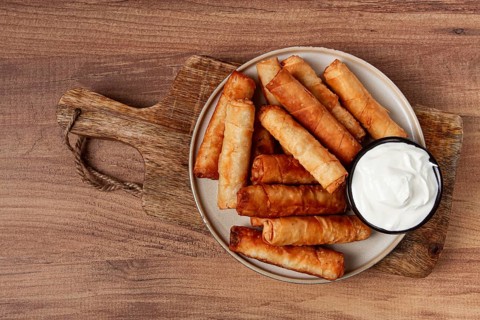 Fried spring rolls with cheese, on a wooden background, with cream sauce, no people
