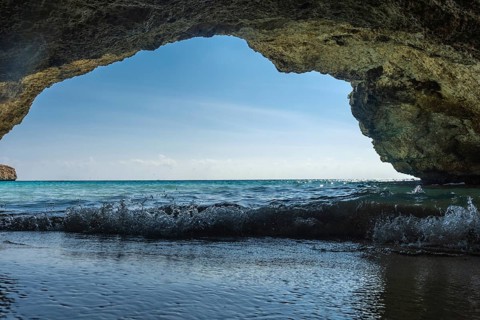 Gentle waves lapping at the shore, viewed from beneath a rocky overhang on a sunny beach in cala