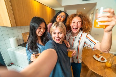 Group of cheerful young multi ethnic friends taking selfie while drinking juice and smiling in