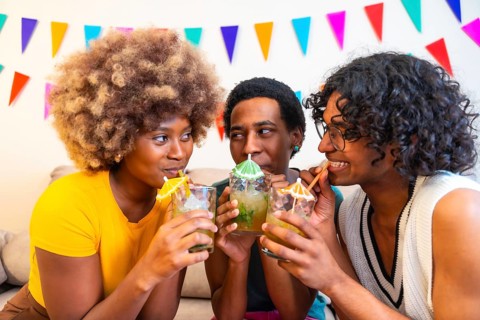 Cool multi-ethnic friends enjoying cocktails drinking sucking with straw and partying at home