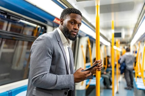 Young businessman using smartphone while commuting on subway train, holding handrail and looking