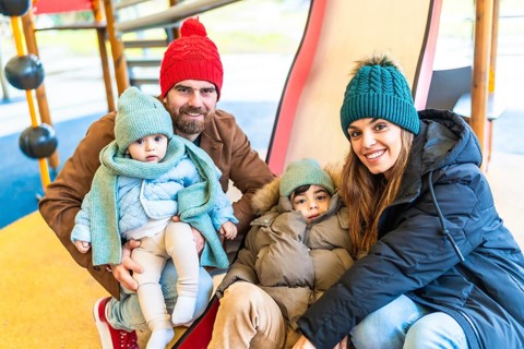 Smiling parents and children wearing winter clothes enjoying a winter day on a playground slide