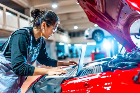 Young female mechanic using a laptop while inspecting a car engine in a professional auto repair