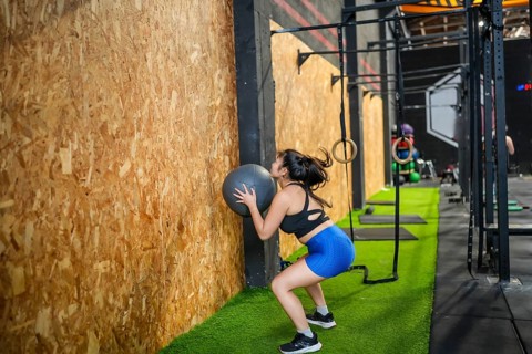 Chinese fit woman training with medicine ball in the gym squatting and throwing up the ball