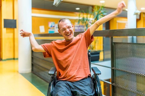 Successful man with disability celebrating in a modern coworking sitting on wheelchair and raising