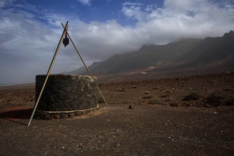 Stone fountain in lonely, barren volcanic landscape near Cofete in front of cloudy mountains,