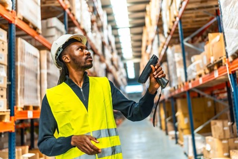 Side view of an african worker scanning package with bar code reader in a distribution warehouse