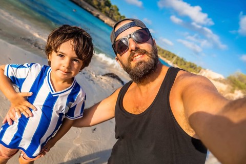 A man and a boy are posing for a picture on a beach. The boy is wearing a blue and white striped