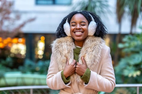 Happy young woman wearing cozy earmuffs and a stylish winter coat, smiling brightly while enjoying